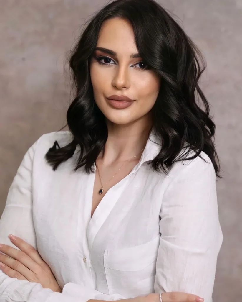 Portrait of Martina Cetaj, PMU artist and trainer, wearing a white shirt with her arms folded